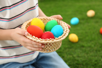 Photo of Cute little boy with basket full of Easter eggs outdoors, closeup