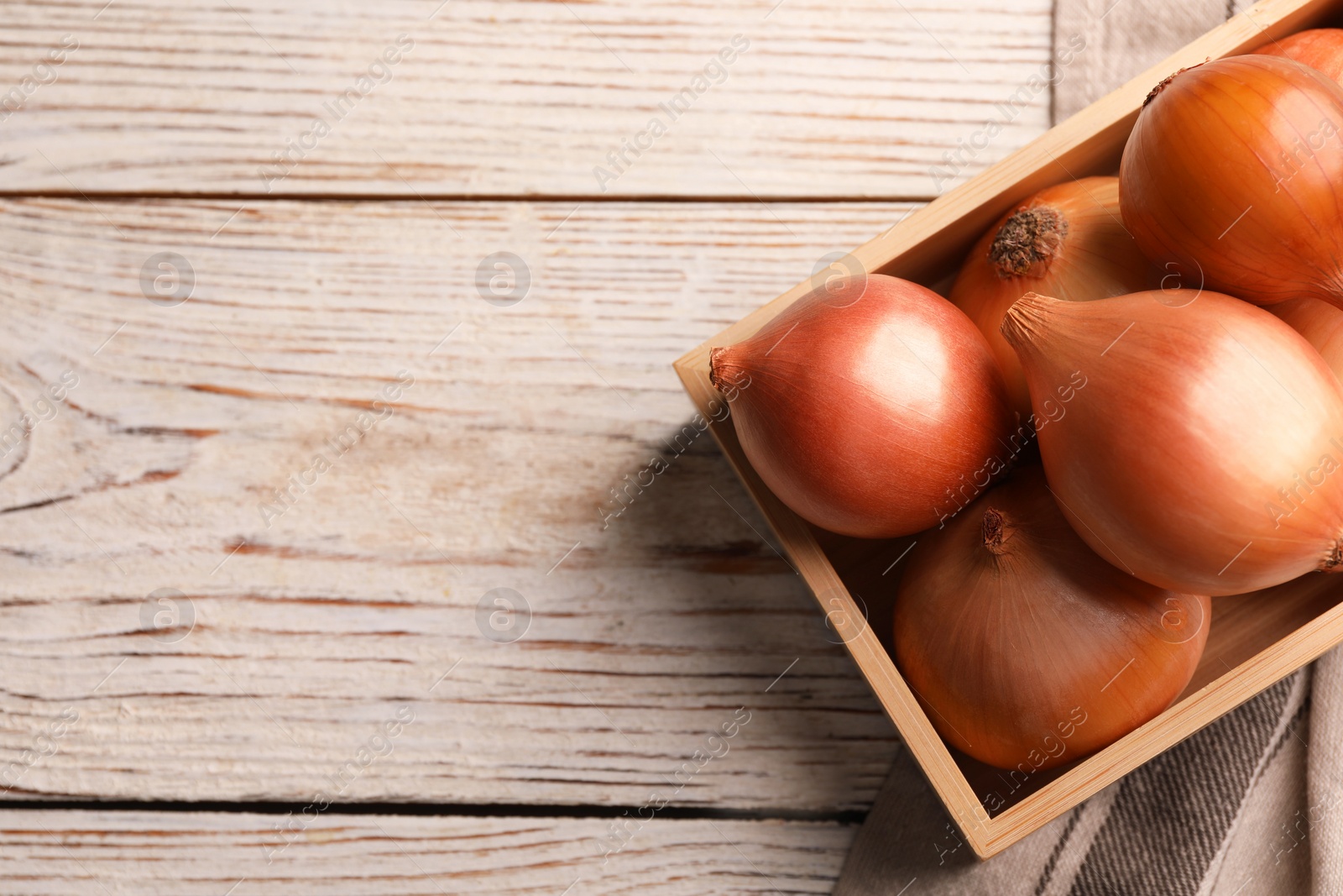 Photo of Crate with ripe onions on white wooden table, top view. Space for text