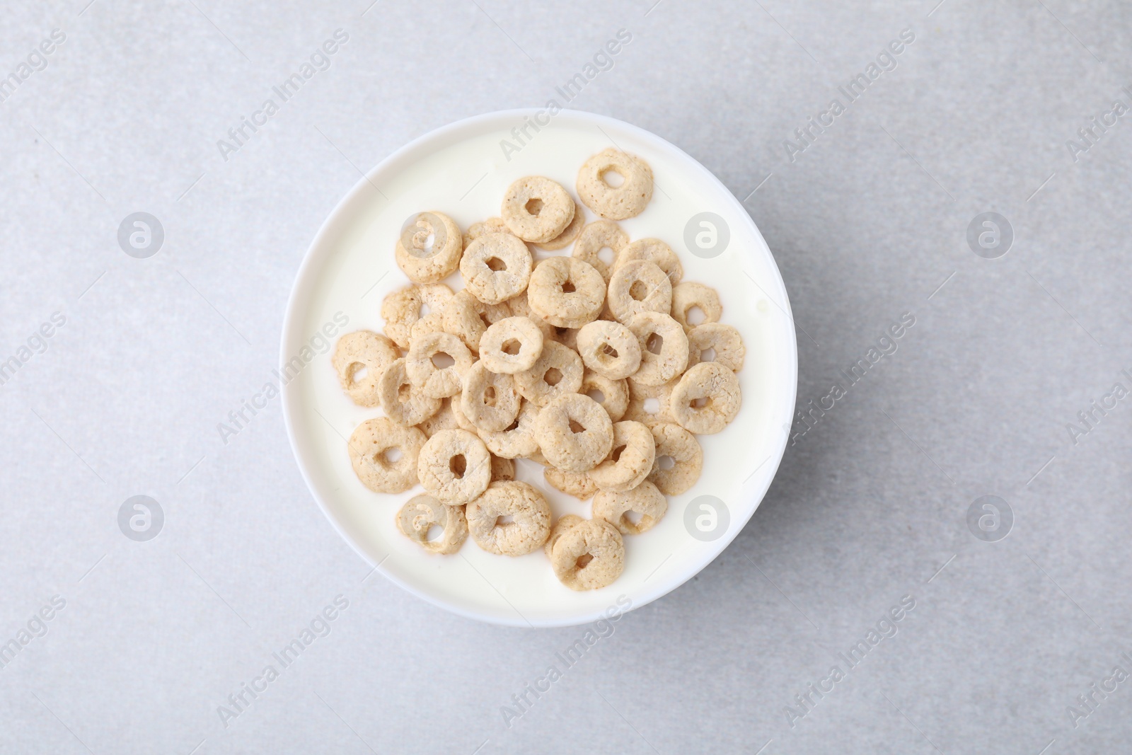 Photo of Breakfast cereal. Tasty corn rings with milk in bowl on grey table, top view