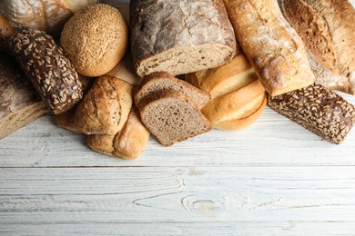 Photo of Different kinds of fresh bread on wooden table, flat lay. Space for text