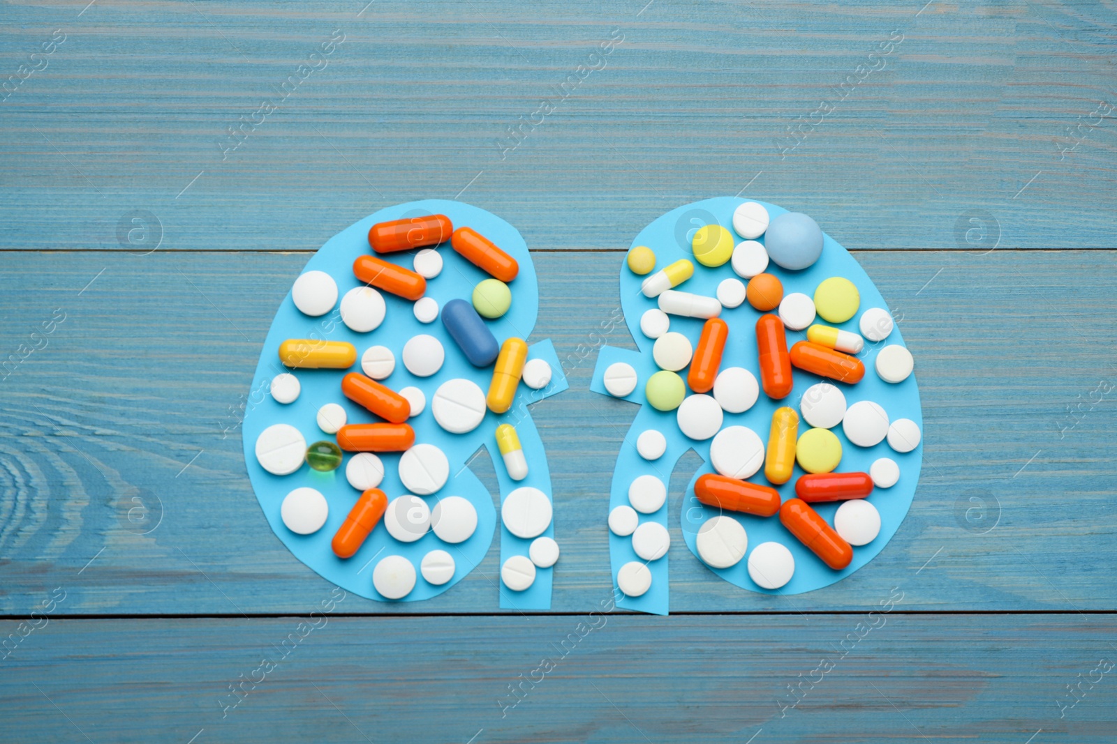 Photo of Paper cutout of kidneys with pills on blue wooden table, top view