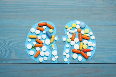 Paper cutout of kidneys with pills on blue wooden table, top view