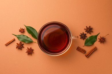 Cup of tea, anise stars, green leaves and cinnamon sticks on brown background, flat lay