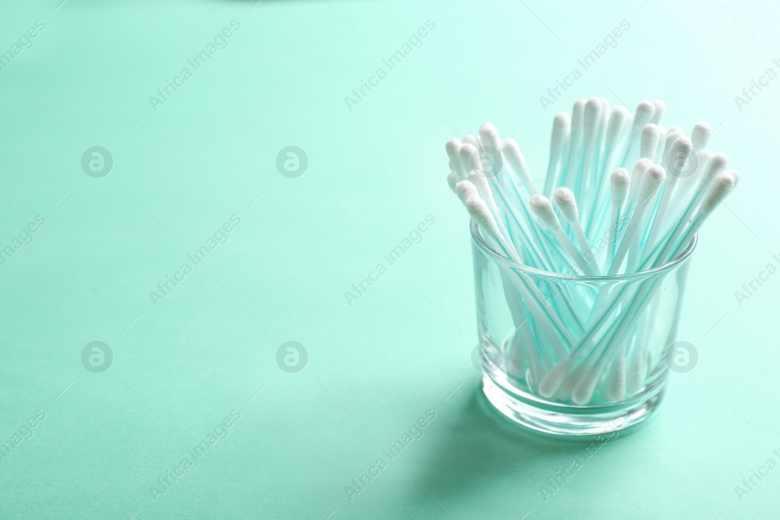 Photo of Glass with cotton swabs on color background. Space for text