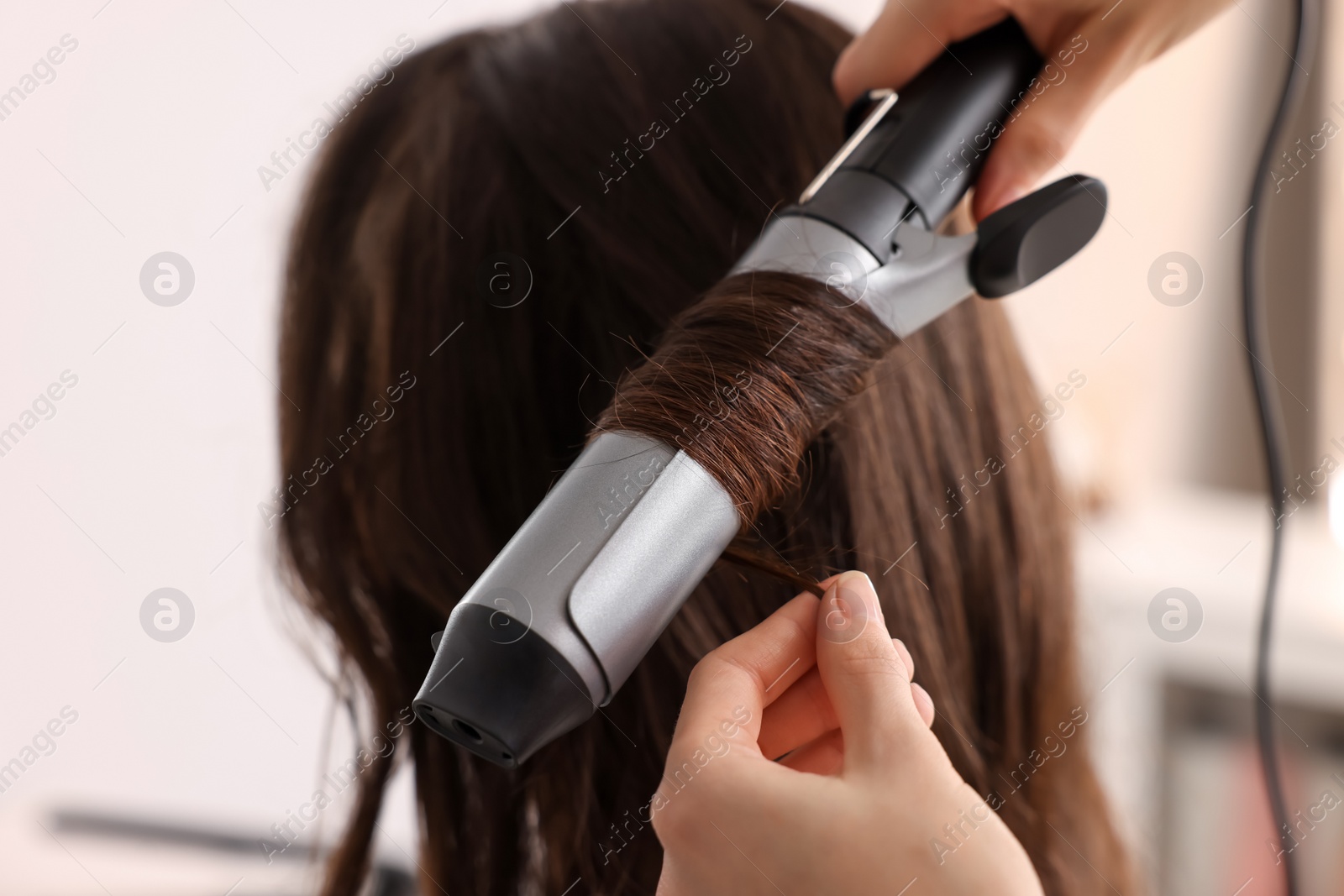 Photo of Hairdresser working with client using curling hair iron in salon, closeup