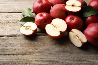 Photo of Fresh red apples and leaves on wooden table, space for text