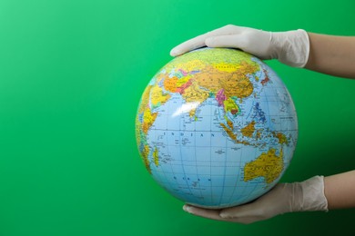 Photo of Doctor in surgical gloves holding globe against green background, closeup. Space for text