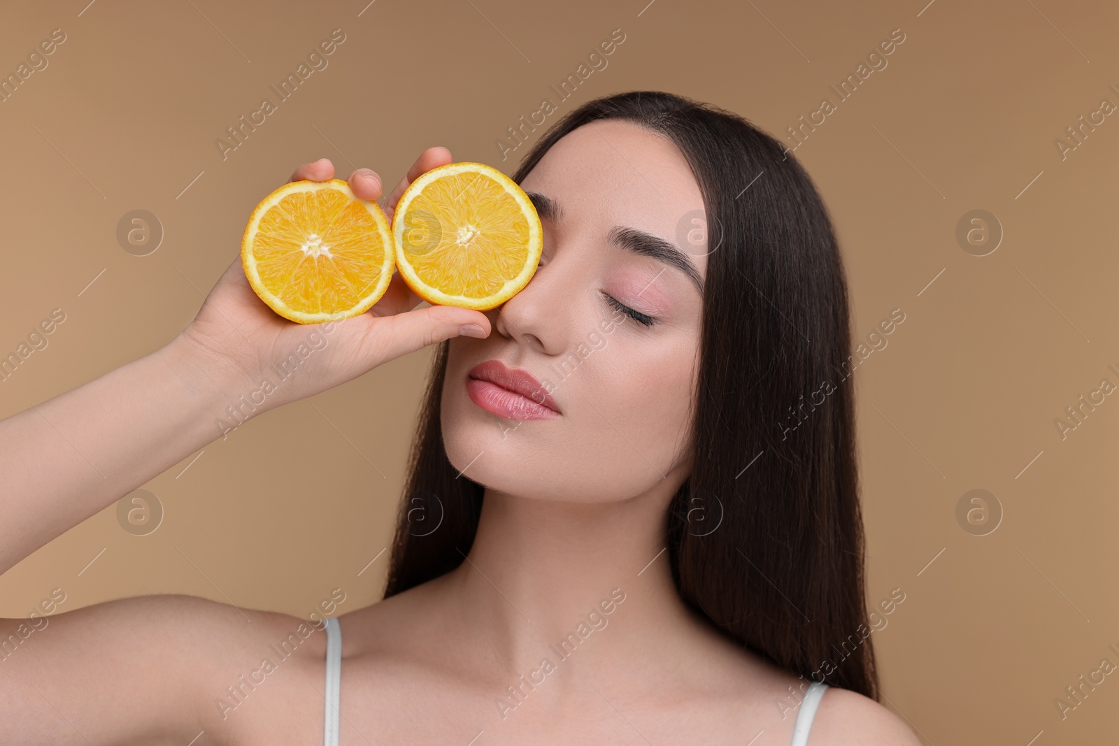 Photo of Beautiful young woman with pieces of orange on beige background