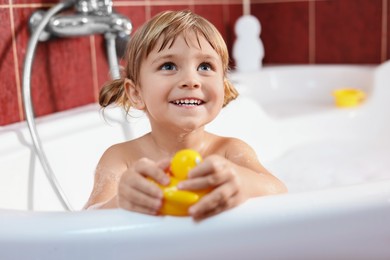 Photo of Smiling girl bathing with toy in tub at home