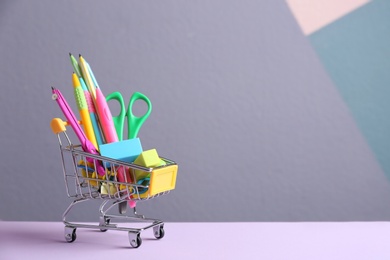 Photo of Small shopping cart with different school stationery on color background. Space for text