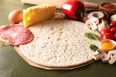 Pizza base and products on green textured table, closeup