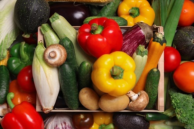 Different fresh vegetables and wooden crate as background, top view