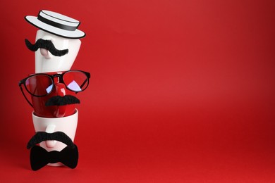 Photo of Men's faces made of cups, fake mustaches, glasses, hat and bow tie on red background. Space for text