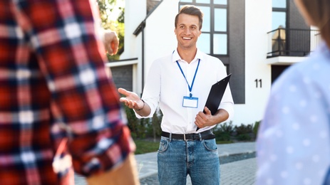 Photo of Real estate agent showing house to young couple outdoors