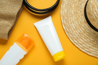 Photo of Suntan products and wicker hat on orange background, flat lay