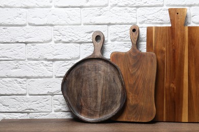 Photo of Different cutting boards on wooden table near white brick wall. Space for text
