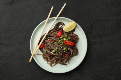 Photo of Tasty buckwheat noodles (soba) with chili pepper, onion and chopsticks on black textured table, top view