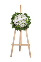 Funeral wreath of flowers with ribbon on wooden stand against white background