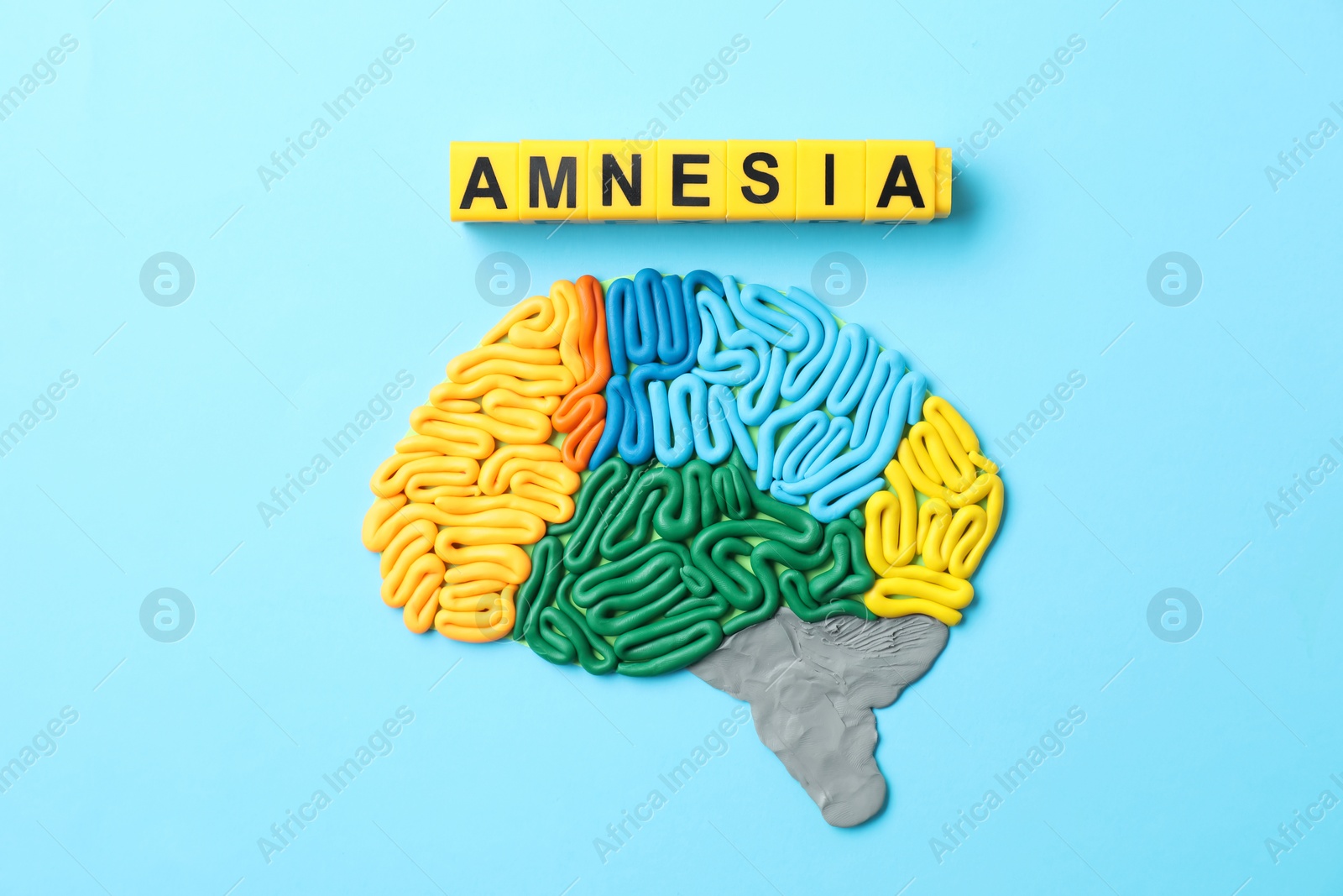 Photo of Word Amnesia and brain with sections made of plasticine on light blue background, flat lay