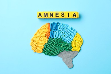 Photo of Word Amnesia and brain with sections made of plasticine on light blue background, flat lay