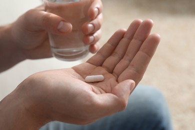 Man with glass of water and pill on blurred background, closeup