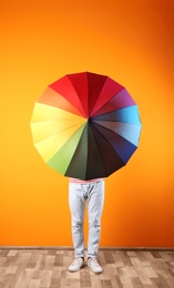 Photo of Man hiding behind rainbow umbrella near color wall