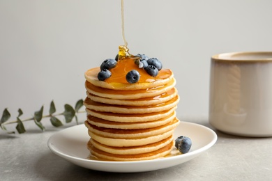 Photo of Pouring honey onto tasty pancakes with berries on table