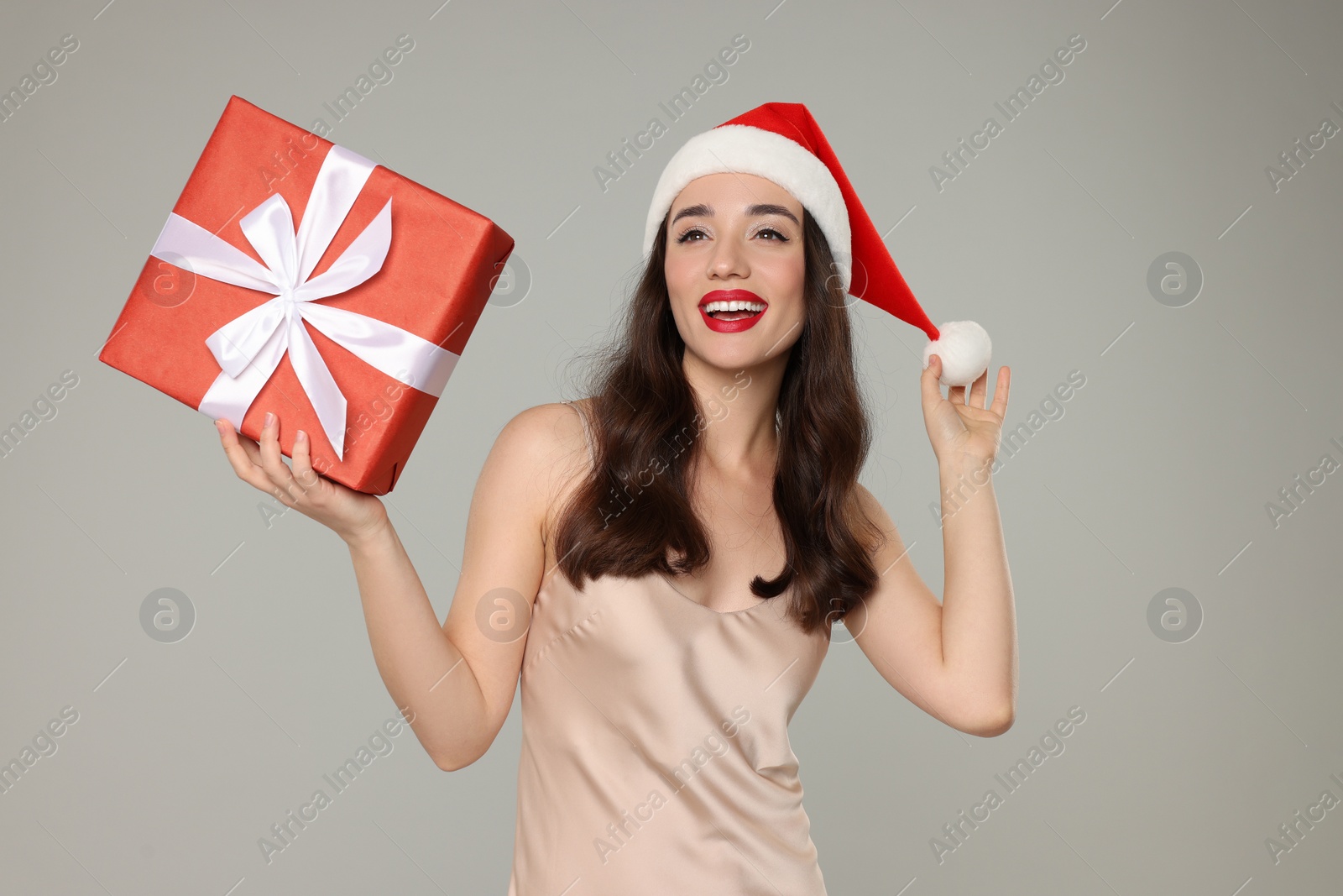 Photo of Beautiful young woman in Santa hat with Christmas gift on grey background