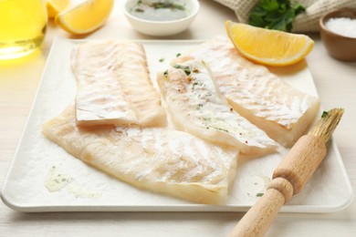 Photo of Fresh raw cod fillets with spices, lemon and brush on white table, closeup