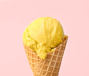 Delicious yellow ice cream in waffle cone on pink background, closeup