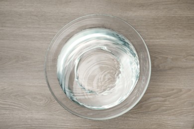 Glass bowl with water on wooden table, top view