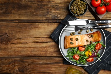 Photo of Tasty cooked salmon with capers and salad served on wooden table, flat lay. Space for text