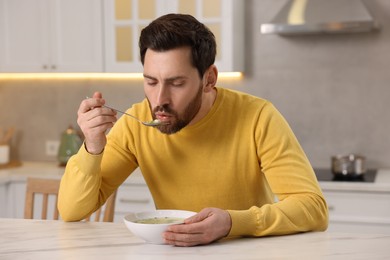 Photo of Man eating delicious chicken soup at light marble table in kitchen