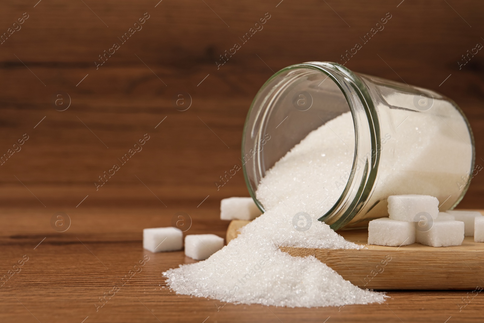 Photo of Overturned jar and white sugar on wooden table, space for text