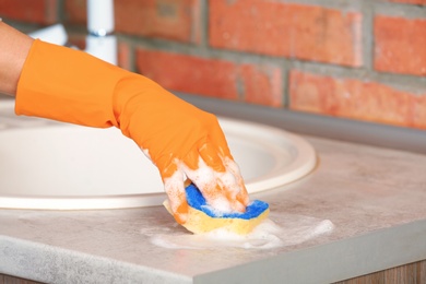 Woman cleaning counter with sponge in kitchen, closeup
