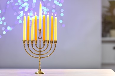 Photo of Hanukkah celebration. Menorah with burning candles on table against blurred lights, space for text