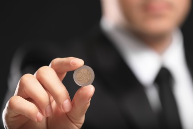 Businessman holding coin on black background, closeup. Space for text