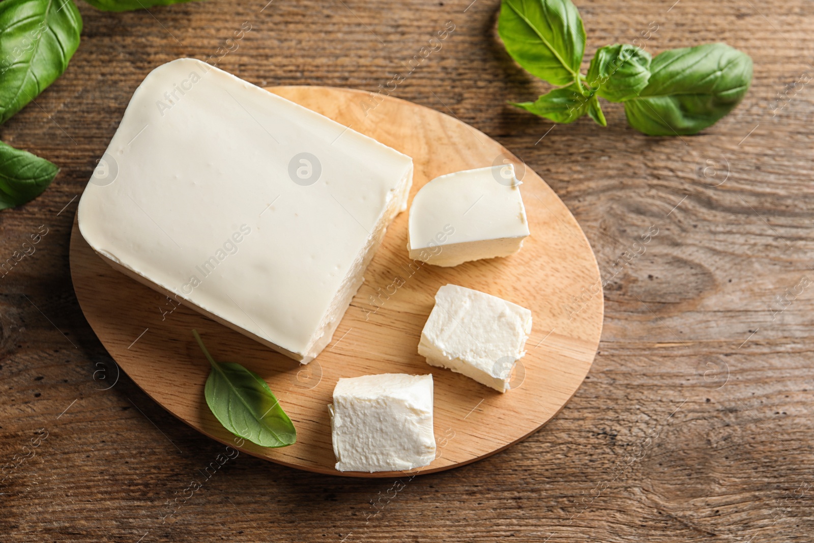 Photo of Board with feta cheese and basil on wooden background, top view