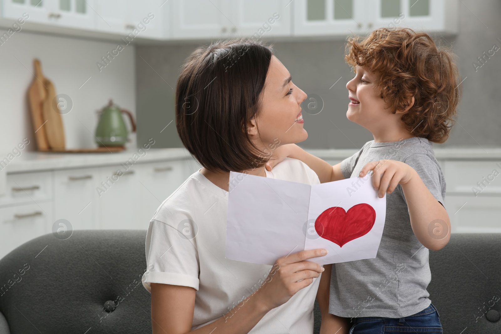 Photo of Little son congratulating his mom with Mother`s day at home. Woman holding greeting card