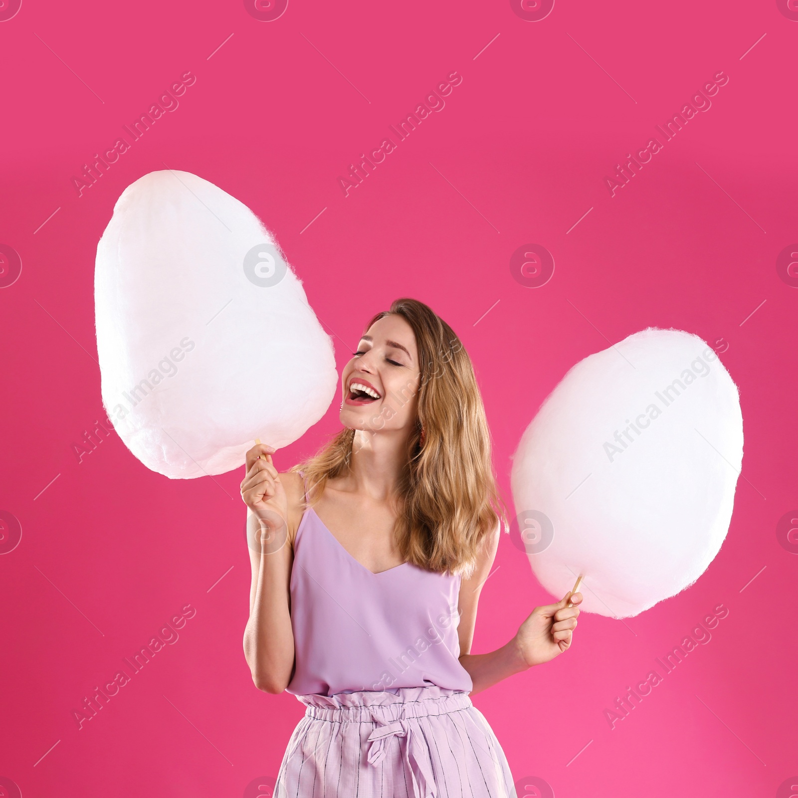 Photo of Happy young woman with cotton candies on pink background