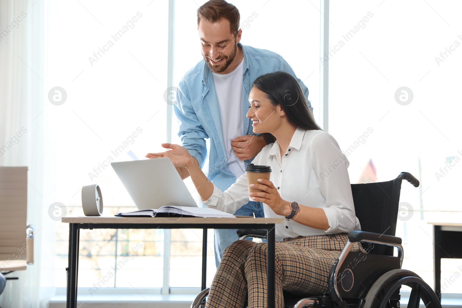 Photo of Young woman in wheelchair with colleague at workplace