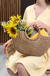 Woman holding beach bag with beautiful bouquet of flowers and books indoors, closeup