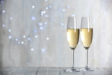 Photo of Sparkling wine in glasses on wooden table against blurred lights, space for text