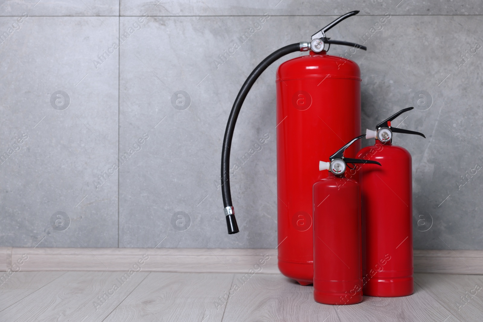 Photo of Fire extinguishers on floor near grey wall, space for text