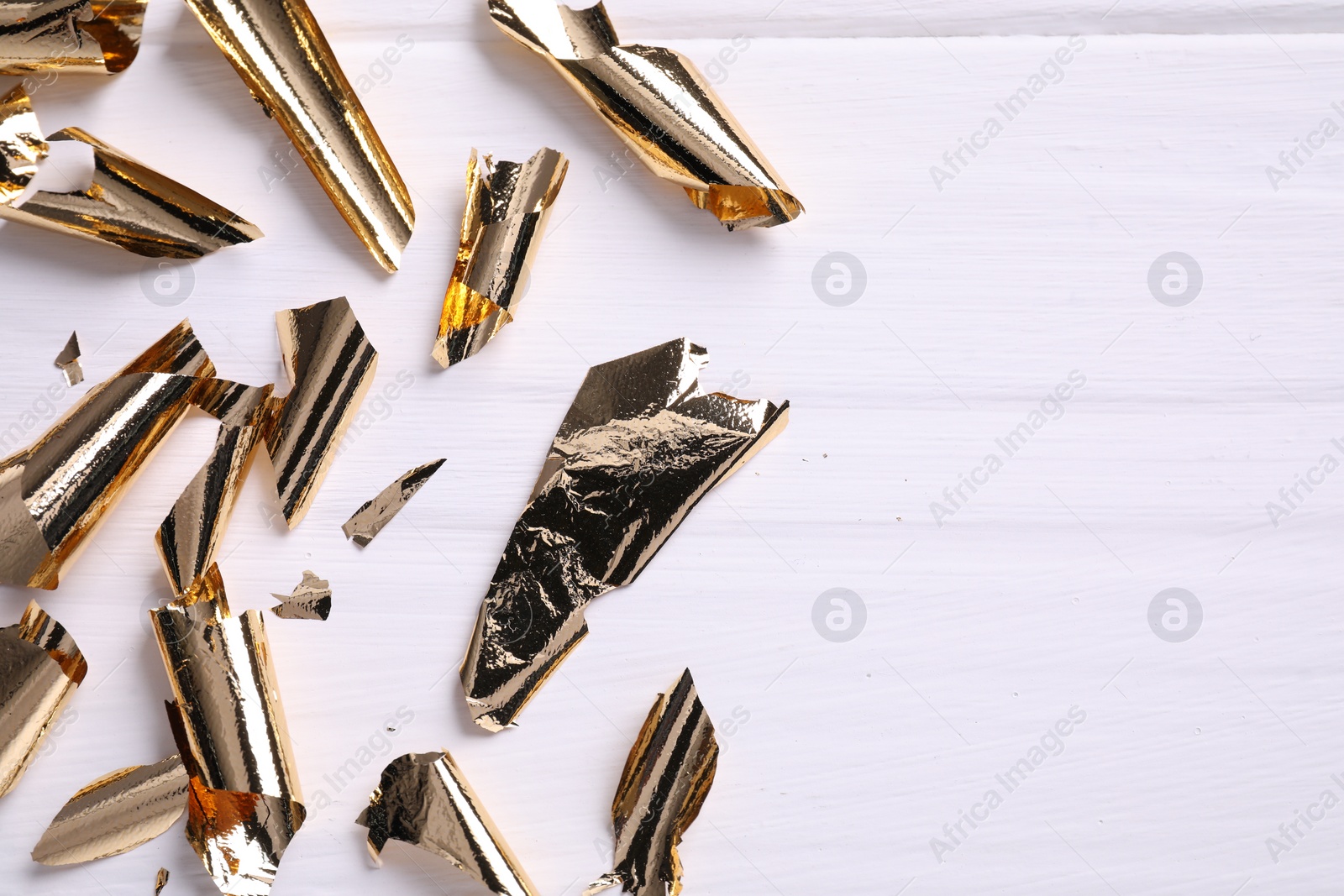 Photo of Many pieces of edible gold leaf on white wooden table, flat lay. Space for text