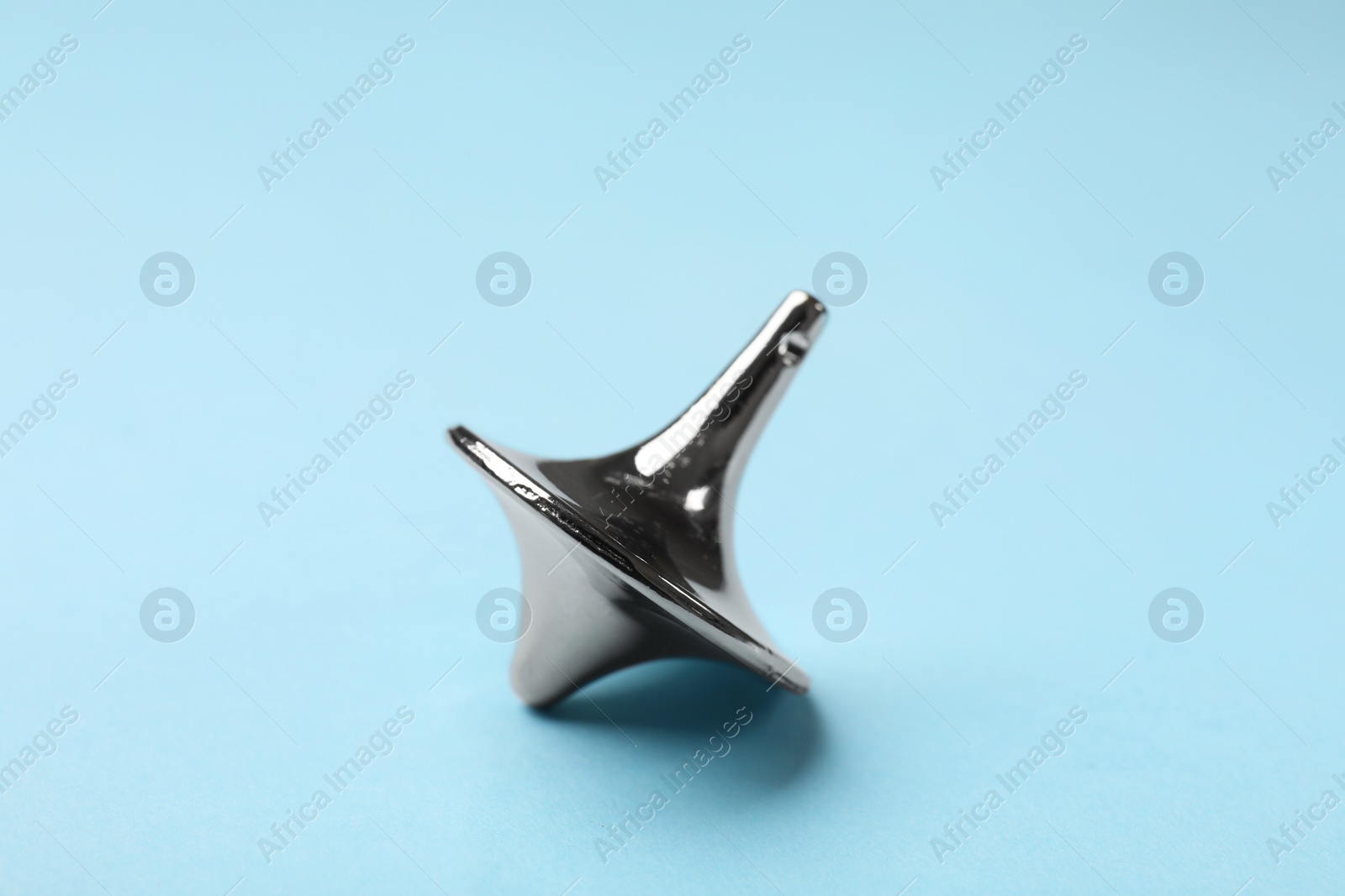 Photo of One silver spinning top on light blue background, closeup