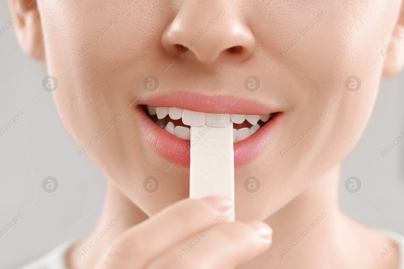 Photo of Woman putting chewing gum piece into mouth on blurred background, closeup