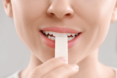 Woman putting chewing gum piece into mouth on blurred background, closeup