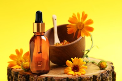 Bottle of essential oil and beautiful calendula flowers on yellow background, closeup. Space for text