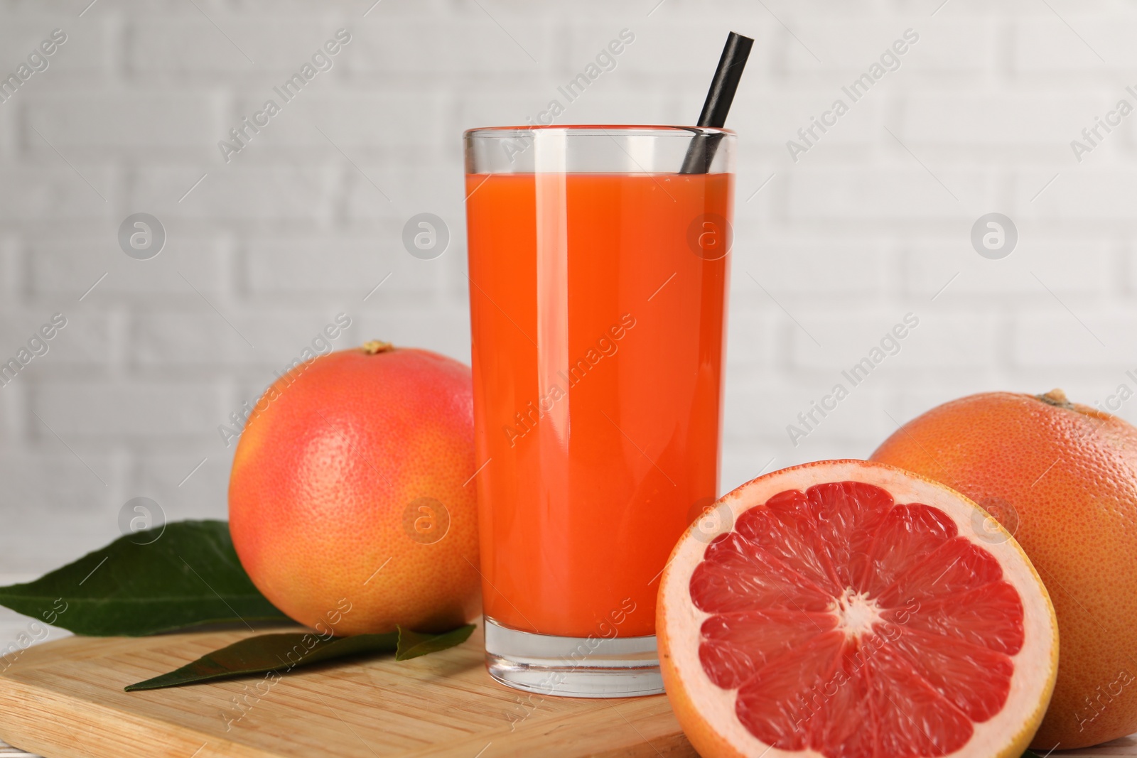 Photo of Tasty grapefruit juice in glass and fresh fruits on table, closeup